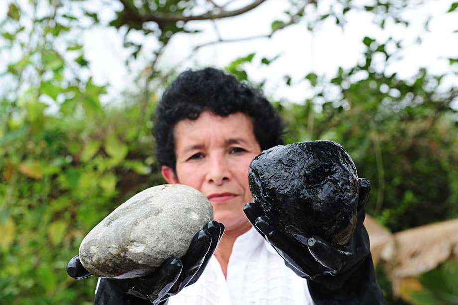 La líder comunitaria Marta Chivatá sostiene dos piedras, una de ellas contaminada, que se encuentran en el punto de vertimiento  de la estación Chichimene. / Nelson Sierra
