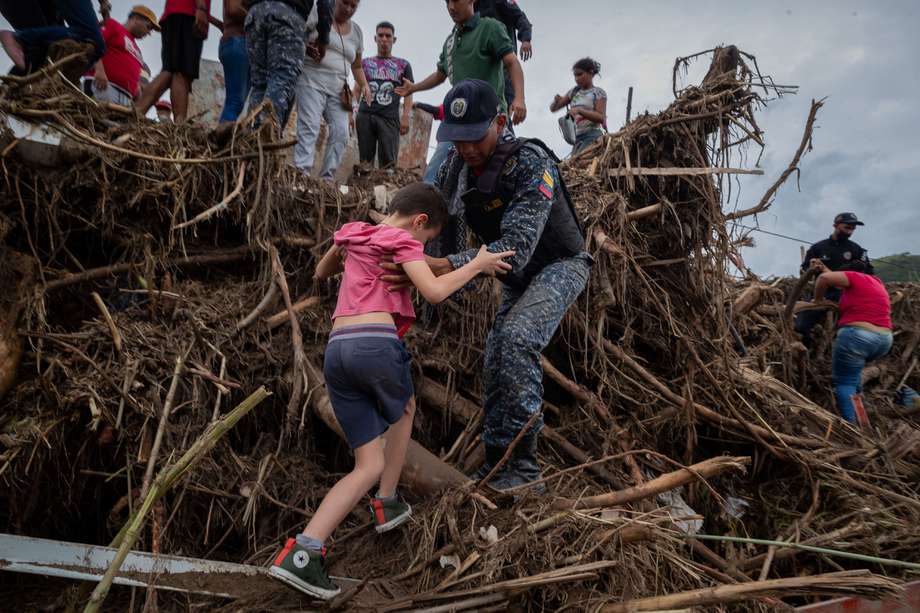 Un policía ayudó a un niño a cruzar por unos destrozos tras el desbordamiento de la quebrada Los Patos, en Las Tejerías, estado Aragua (Venezuela). 
