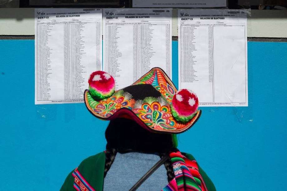 Una mujer quechua vestida con atuendo típico busca su número de cédula en una lista de mesas electorales en Puno, Perú.