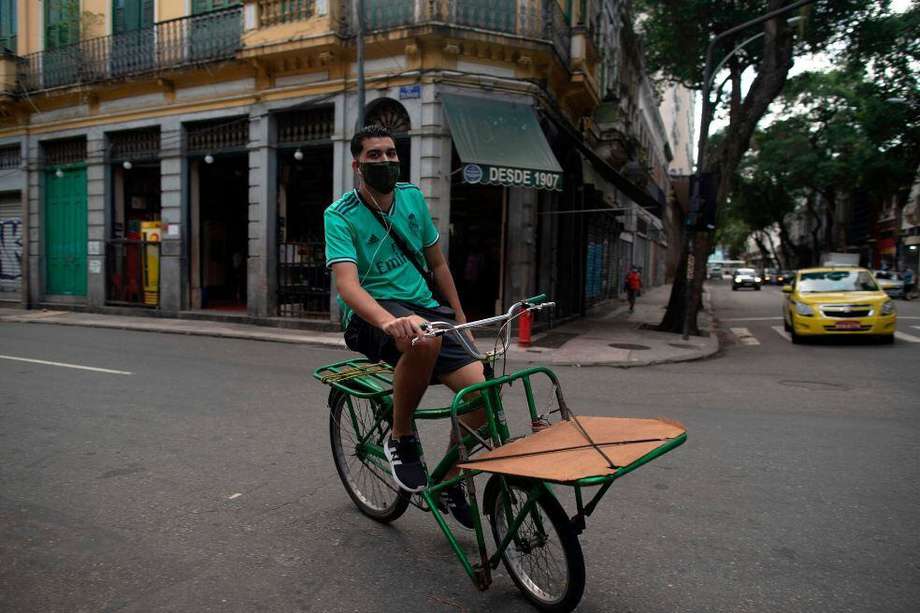 Un hombre que lleva una máscara facial monta una bicicleta en el barrio de Lapa en Río de Janeiro, Brasil, el 2 de julio de 2020 luego de que los bares y restaurantes de la ciudad reabrieron sus puertas después de más de tres meses. / AFP