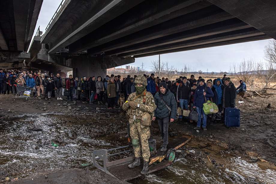 Un militar ucraniano hace guardia mientras los residentes intentan cruzar un puente destruido para huir de la ciudad de Irpin, región de Kiev. Irpin tuvo fuertes enfrentamientos durante casi una semana entre los militares ucranianos y rusos, lo que obligó a miles de personas a escapar.