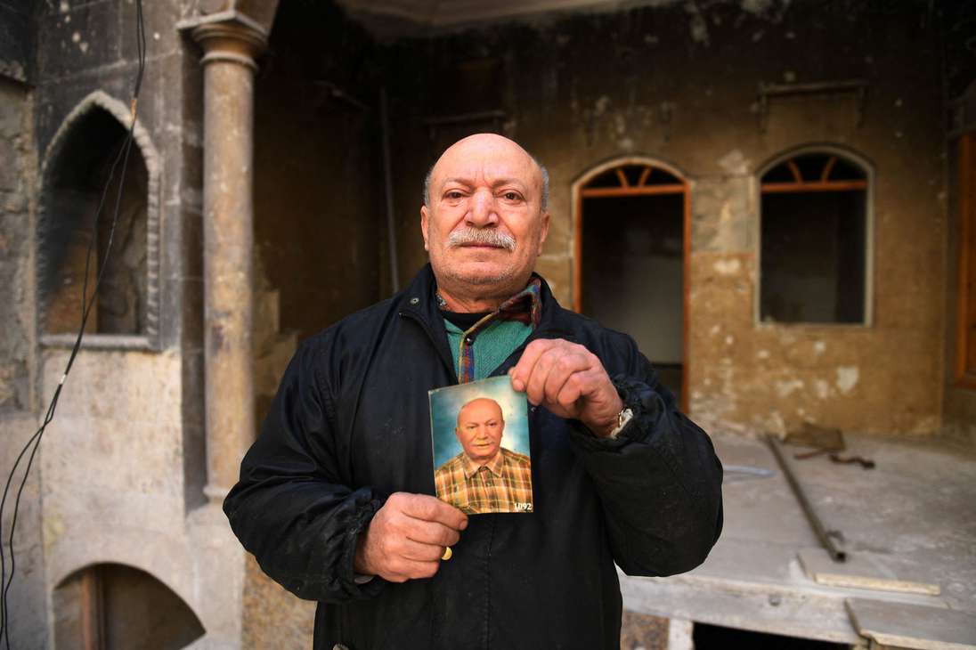 Ahmed Nashawi, también conocido como Abu Abdo, posa con un retrato de sí mismo de hace diez años atrás frente a su casa destruida en la ciudad de Alepo, en el norte de Siria, el 22 de febrero de 2021. El hombre de unos cincuenta años, una vez uno de los pescaderos más populares de la ciudad, dijo que su casa y su tienda en la plaza Sahat al-Hatab fueron destruidas en enfrentamientos entre rebeldes y combatientes progubernamentales en 2015.