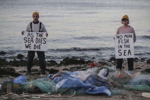 Los activistas de Ocean Rebellion sostienen pancartas que dicen "A medida que el mar muere, nosotros morimos" y "No más peces en el mar" mientras organizan una protesta en Terreiro do Paco en Lisboa el 27 de junio de 2022, antes de la apertura de la Conferencia de la ONU sobre los Océanos.  (Foto por CARLOS COSTA / AFP)