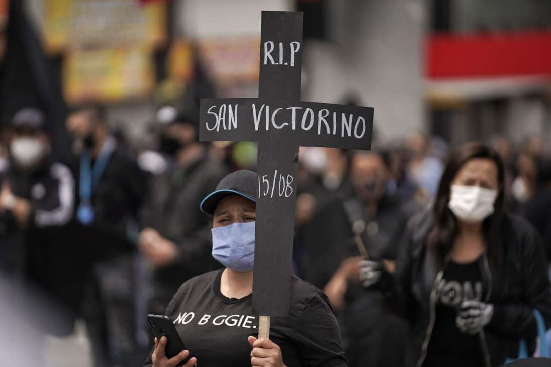 Una mujer sostiene una cruz negra, hecha en cartulina, en la que se lee RIP San Victorino.