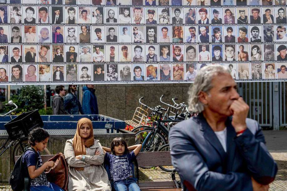 Una familia se sienta frente a una pancarta que muestra retratos de víctimas del Genocidio de Srebrenica en  La Haya.