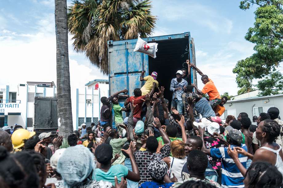 Un hombre arroja una bolsa de arroz a una multitud de víctimas del terremoto reunidas para la distribución de alimentos y agua en el cruce de "4 Chemins" en Les Cayes