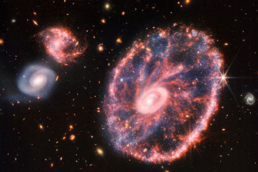 La potente mirada infrarroja del telescopio James Webb ha logrado una instantánea detallada de la Galaxia Rueda, pero también de dos galaxias compañeras más pequeñas con un telón de fondo de muchas otras galaxias.