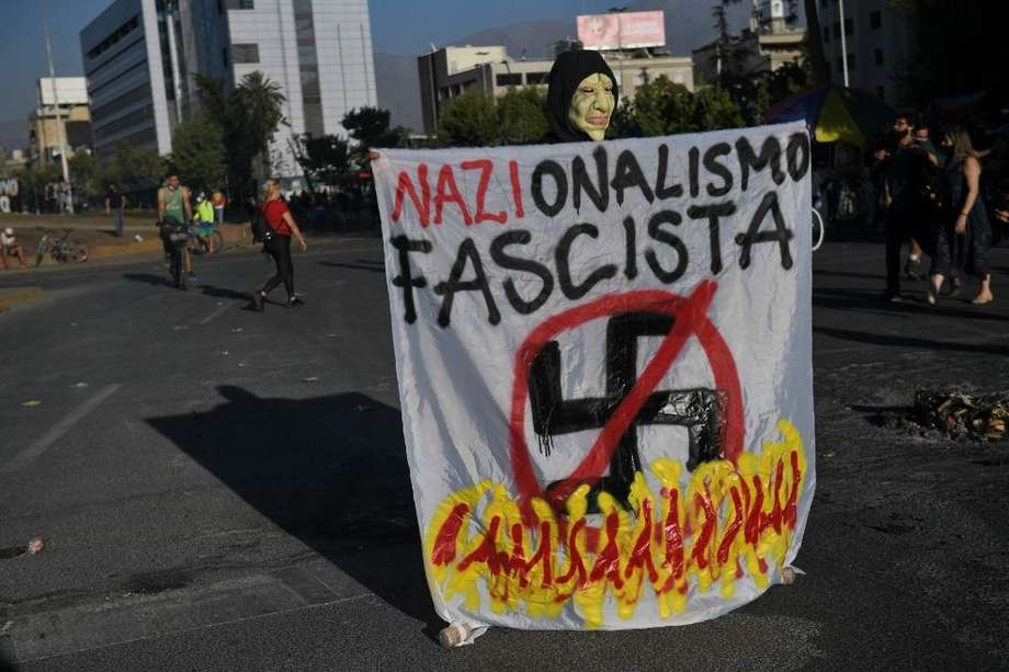 Un manifestante enmascarado sostiene un cartel contra el candidato presidencial de derecha chileno José Antonio Kast, en la Plaza Italia en Santiago.