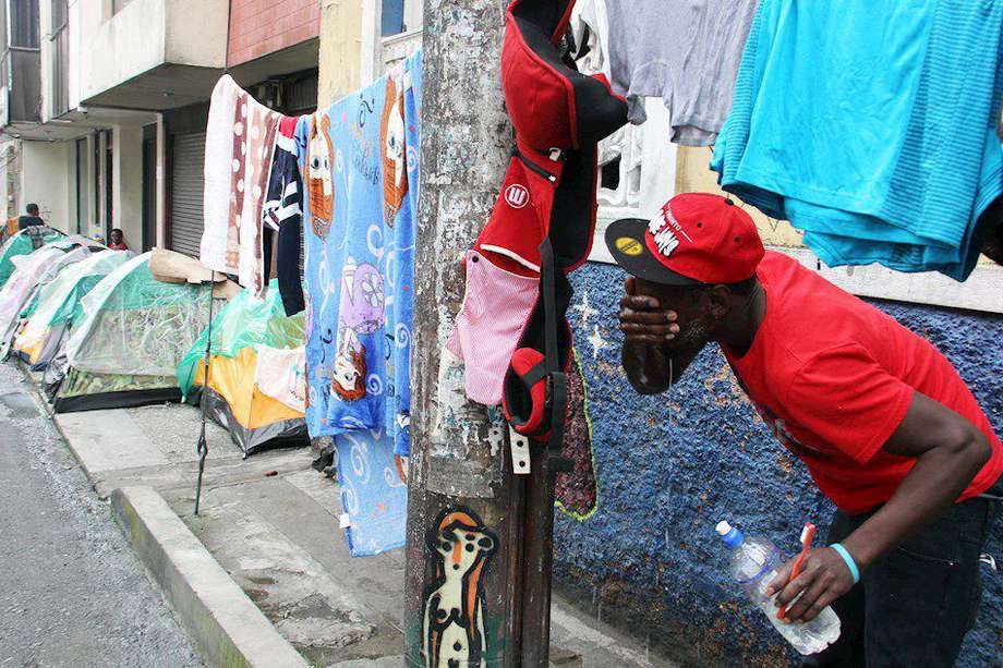 Un migrante haitiano en ruta hacia Norteamérica se lava la cara este martes 7 de julio mientras cuida su ropa en una calle de Pasto. Sebastián Castro- EFE