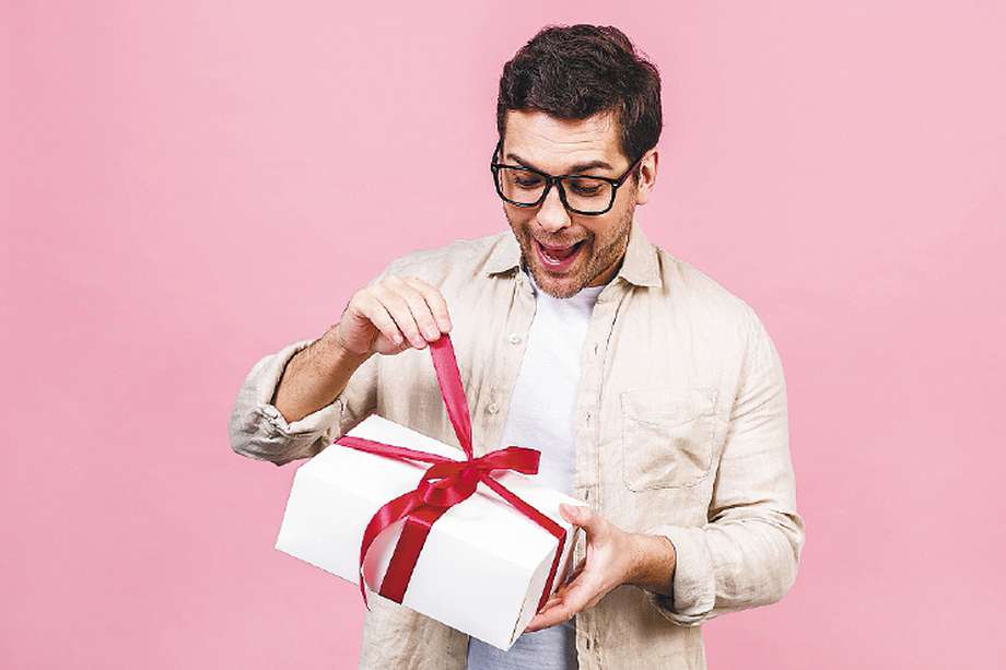 Holiday concept. Portrait of a young man opening gift box isolated over pink background.