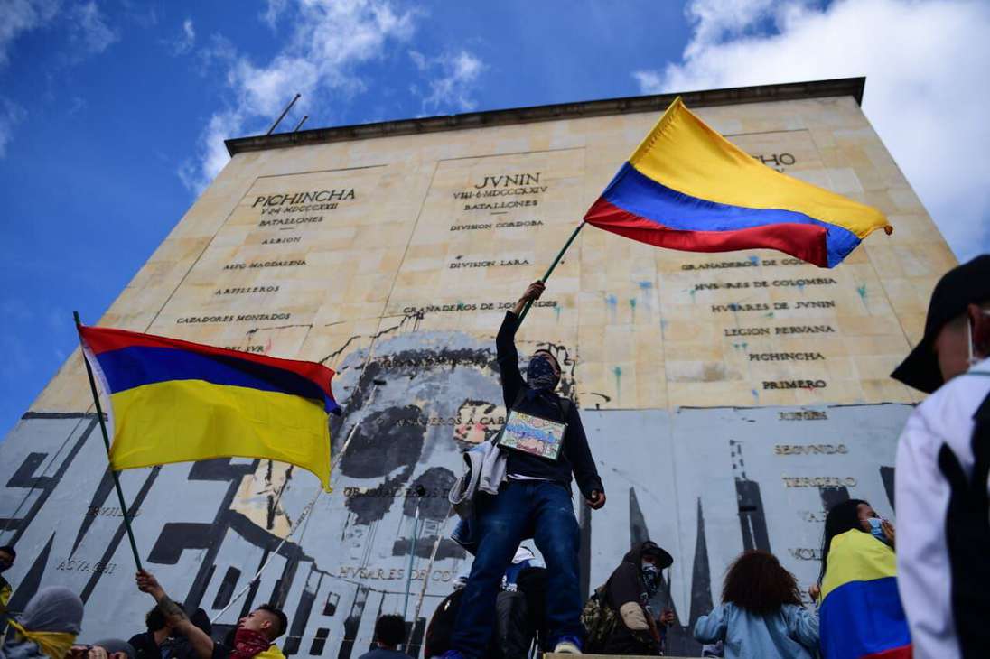Un hombre sostiene una bandera de colombia frente al monumento de Héroes