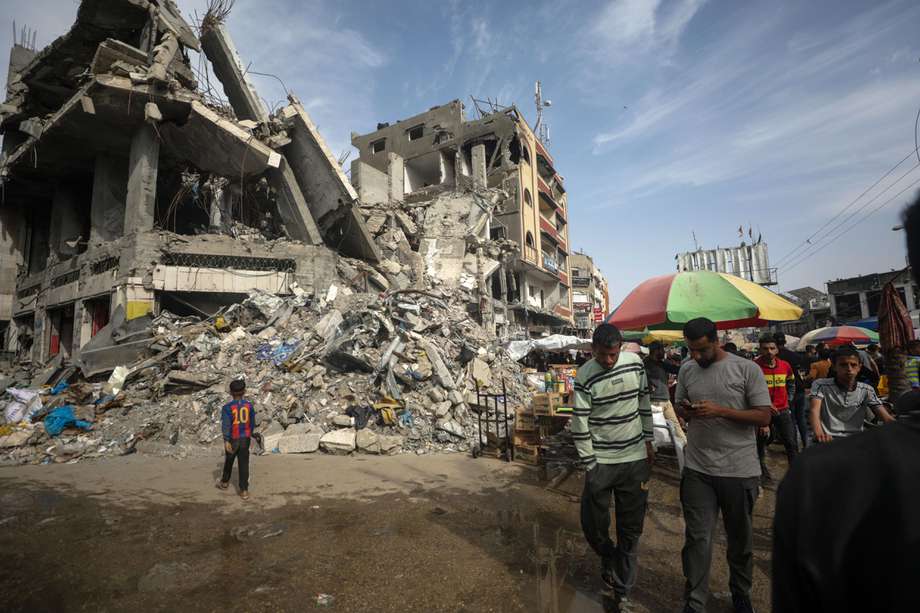 Palestinos pasan junto a quioscos instalados junto a edificios destruidos el último viernes del Ramadán a lo largo de una calle en el campo de refugiados de Al Nusairat, Franja de Gaza, el 5 de abril de 2024.
