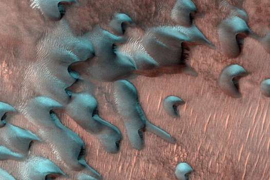 Imagen del Mars Reconnaissance Orbiter de la NASA muestra dunas de arena moviéndose por Marte. La escarcha invernal cubre la mitad más fría, orientada al norte, de cada duna.