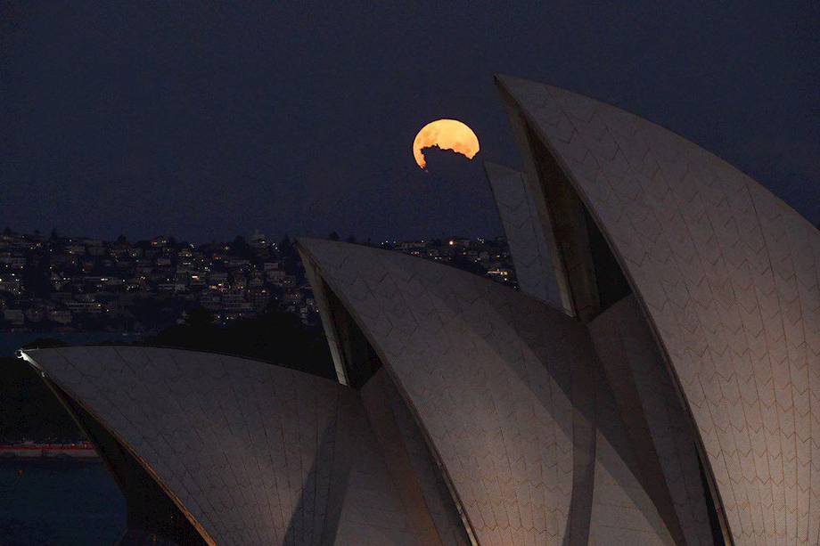 La súper luna rosa se eleva detrás de las velas de la ópera de Sydney, Australia.