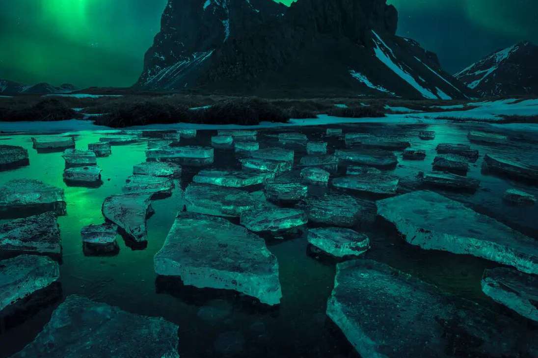 La imagen muestra la aurora boreal bailando, reflejada en un pequeño lago helado sobre la montaña Eystrahorn.