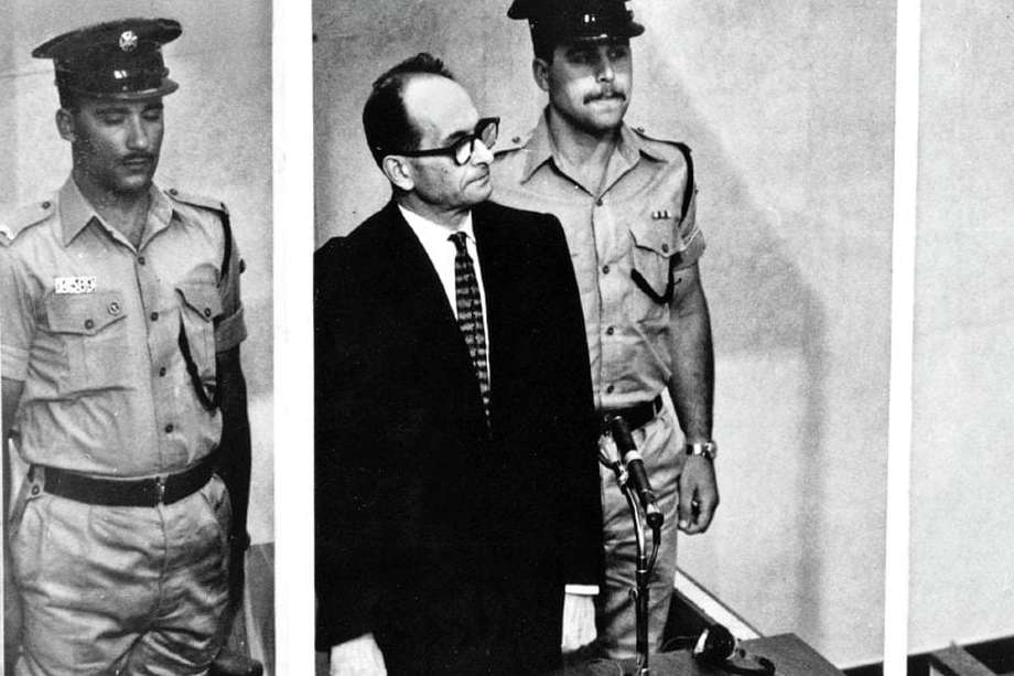 Adolf Eichmann de pie en su jaula de cristal, flanqueado por guardias, en la sala del tribunal de Jerusalén donde fue juzgado en 1961 por ser el "arquitecto del Holocausto", el coordinador de la política de genocidio de los nazis. Huyó de Alemania y fue capturado en Argentina por el Mossad y llevado a Israel para ser juzgado y ahorcado.