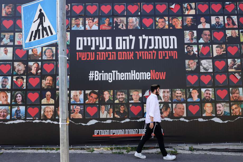 Un hombre pasa junto a un cartel de gran tamaño que muestra imágenes de rehenes israelíes retenidos por Hamás en la Franja de Gaza y que dice "Mírenlos a los ojos, debemos traerlos a casa ahora", en Jerusalén, el 3 de abril de 2024.
