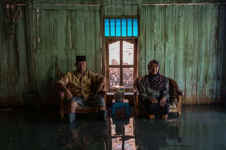 Abdul Muid (60) y su esposa Muniah (55) posan dentro de su casa inundada debido al aumento del nivel del mar. Abdul y su familia han estado viviendo en esta casa y viviendo con las inundaciones durante unos diez años. No tiene dinero para mudarse a otra casa, más lejos del mar. En la ciudad de Java, Indonesia.