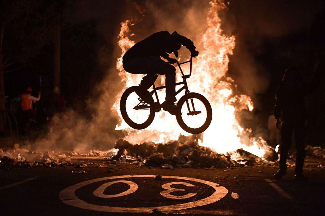La silueta de un hombre en bicicleta frente a una llamarada de fuego.