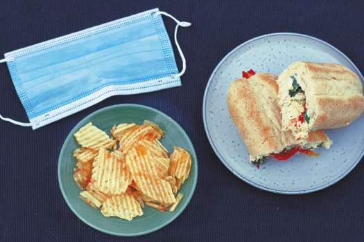 A sandwich baguette and potato chips / crisps and a medical face mask