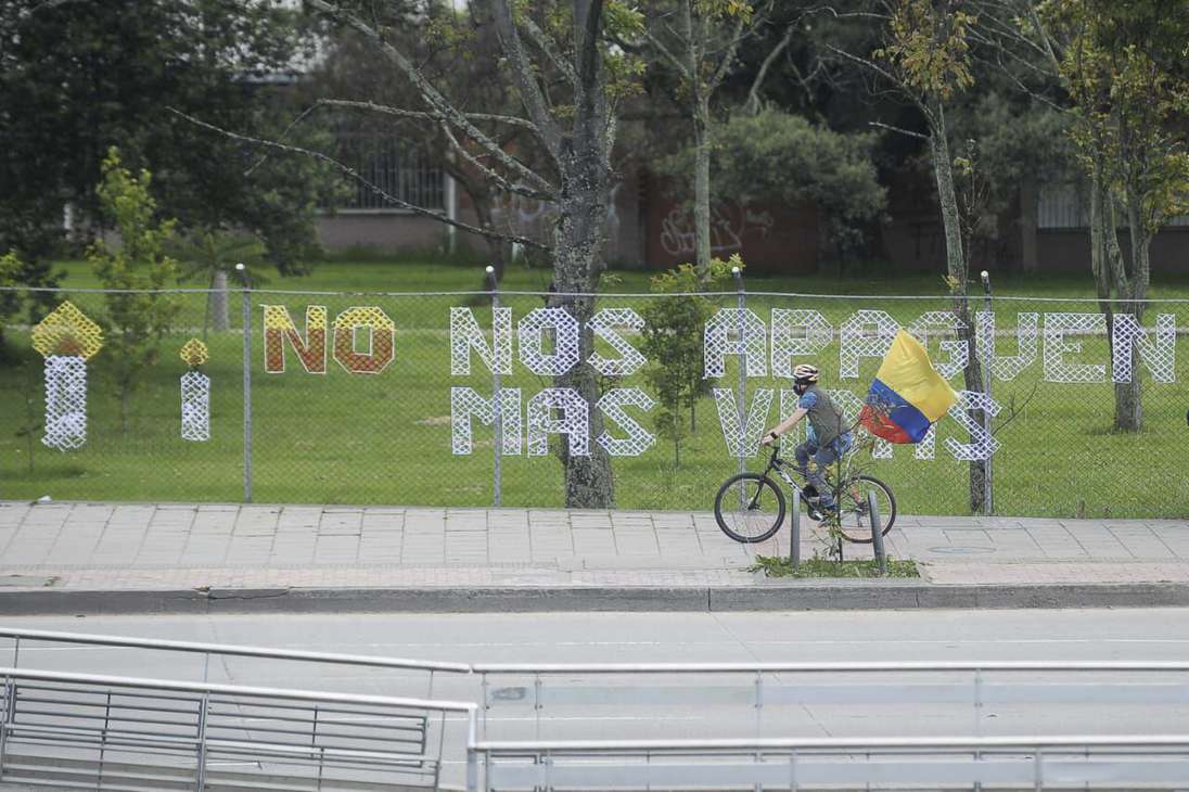 Un hombre en bicicleta pasando por el frente de un letrero que dice: no nos apaguen más vidas