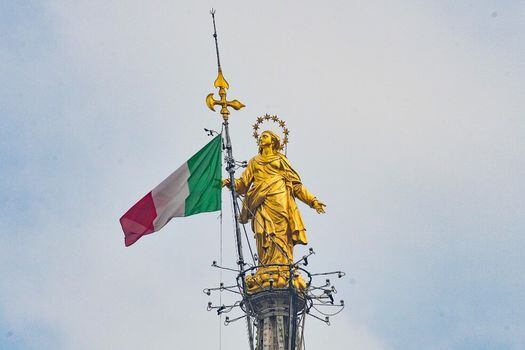 Una bandera italiana ondeando junto a la Madonnina, una estatua de cobre dorado de Giuseppe Perego, que representa a la Madonna Assunta y colocada en 1774 en la torre principal de la catedral de Milán se convirtió en el símbolo de la ciudad, Milán, Italia. / EFE