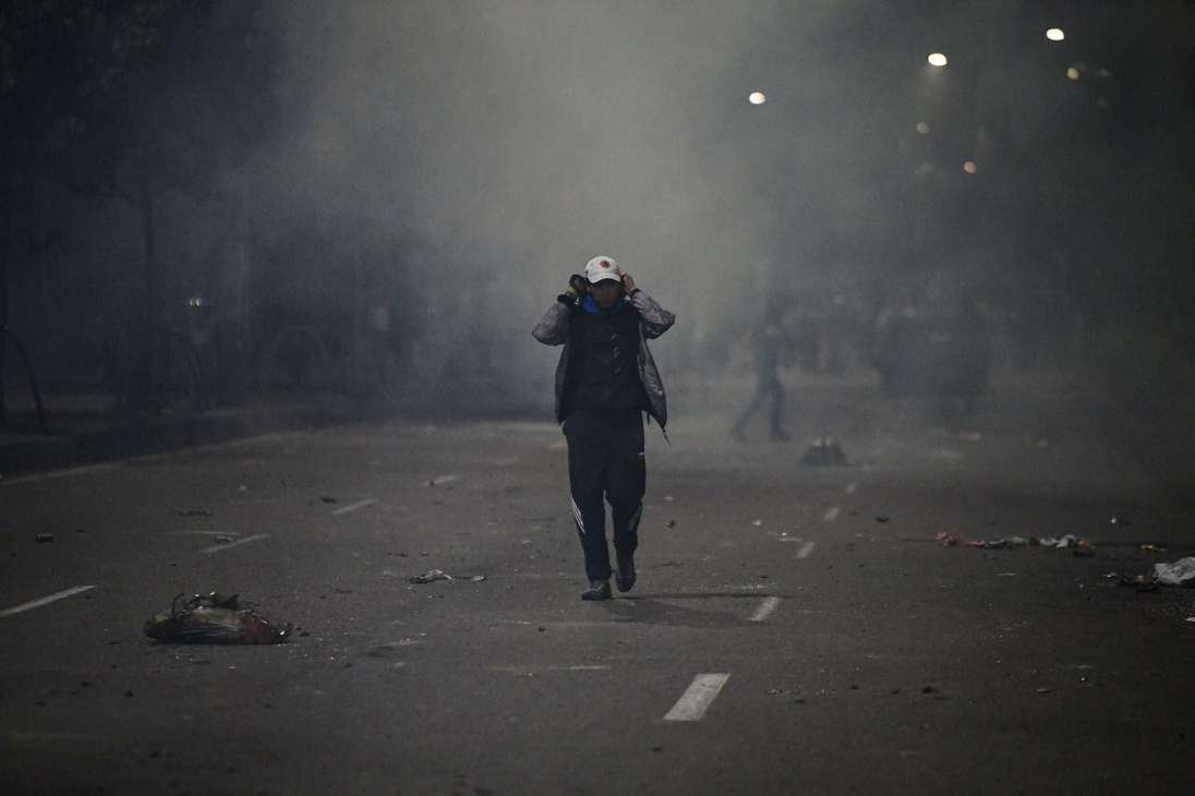 Un hombre con las manos en las orejas caminando entre gases lacrimógenos.