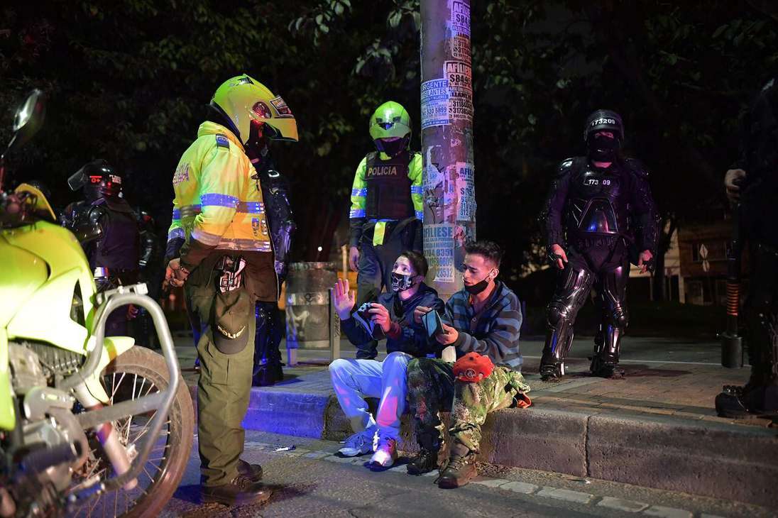 Un Policía habla con dos personas sentadas en una acera