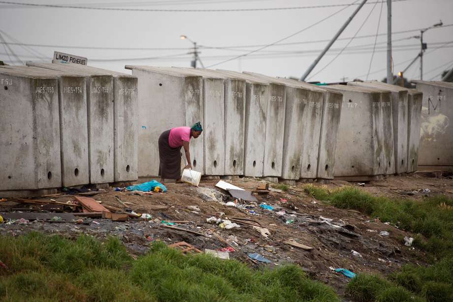 Una mujer tira aguas residuales junto a una hilera de sanitarios en un asentamiento informal en Langa, un municipio mayoritariamente empobrecido, a unos 10 km del centro de Ciudad del Cabo, el 12 de noviembre de 2017, en plena crisis de agua.