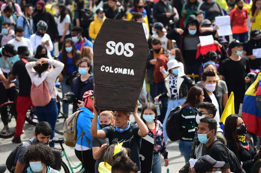 Varias personas marchando. una de ellas carga un ataúd de cartón que dice SOS Colombia