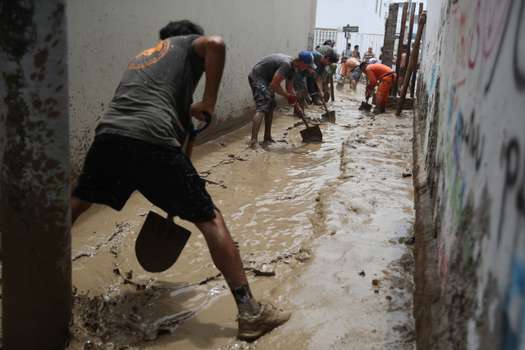 People help to remove the mud in a street affected by the rains today, in the resort of Punta Hermosa in the south of Lima.