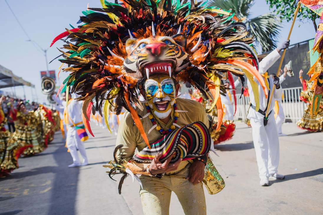 Hombre disfrazado de tigre usando una máscara con colores llamativos y un sombre vueltiao en su mano.
