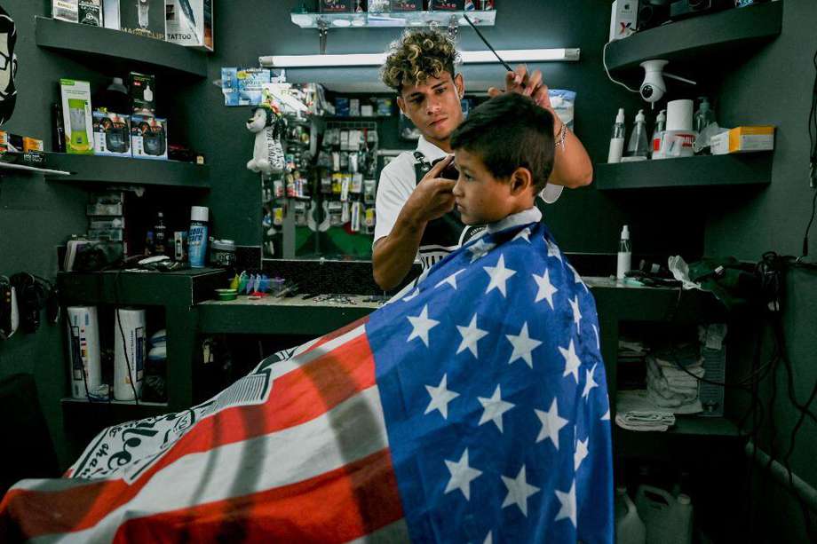 Wilmer Rodríguez trabaja en la barbería “La Bendición”. En su trabajo, como una premonición o estímulo para migrar, los cobertores que coloca a sus clientes representan la bandera de Estados Unidos.