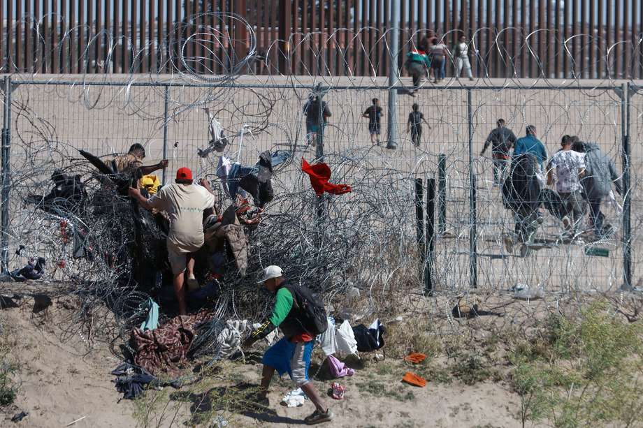 Migrantes cruzan una alambrada de navajas y púas en la frontera que divide a México con Estados Unidos, en Ciudad Juárez.