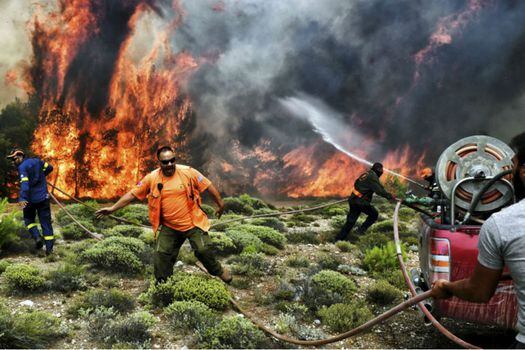 Voluntarios y bomberos se esfuerzan por apagar el fuego en Kineta, cerca a Atenas, en donde las llamas consumieron hogares y carros enteros y ya dejan un saldo de 79 muertos.  / Valerie Gache / AFP