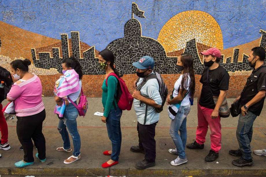 Un grupo de venezolanos hace fila para abordar un autobús junto a un mural que representa el edificio de la Asamblea Nacional en Caracas.