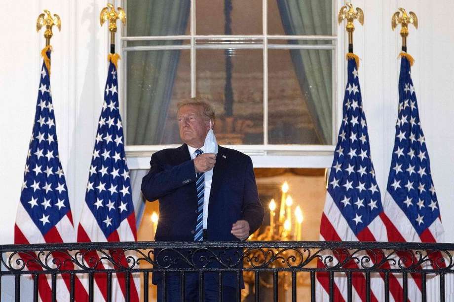 El presidente Donald Trump se retira su tapabocas tras su regreso a la Casa Blanca el lunes en la tarde.