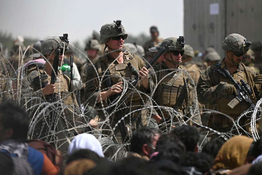 Los soldados estadounidenses montan guardia detrás de un alambre de púas mientras los afganos se sientan en una carretera cerca de la parte militar del aeropuerto en Kabul el 20 de agosto de 2021