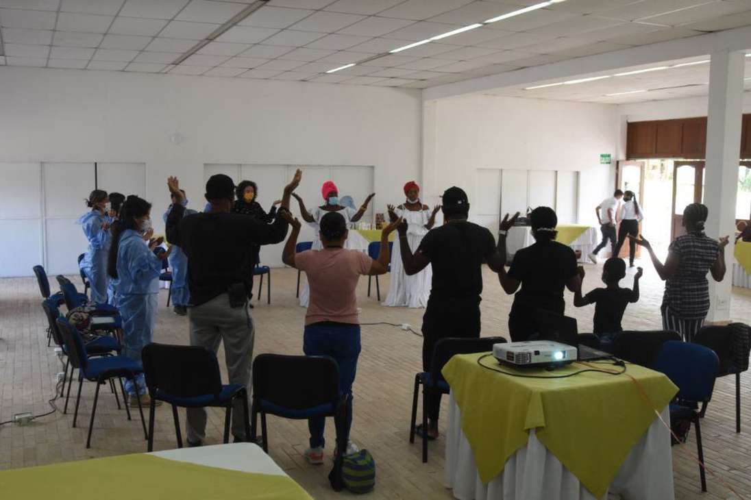 un grupo de aproximadamente 20 personas se encuentran organizados en un circulo, mientras levantan sus manos en signo de oración.
