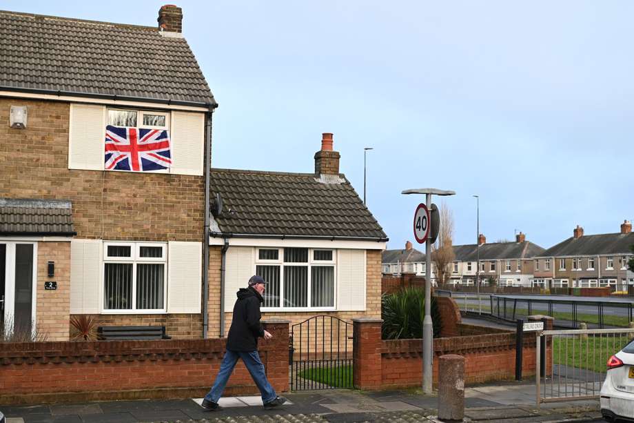Un hombre camina frente a una casa con una bandera de Reino Unido colgada en la ventana