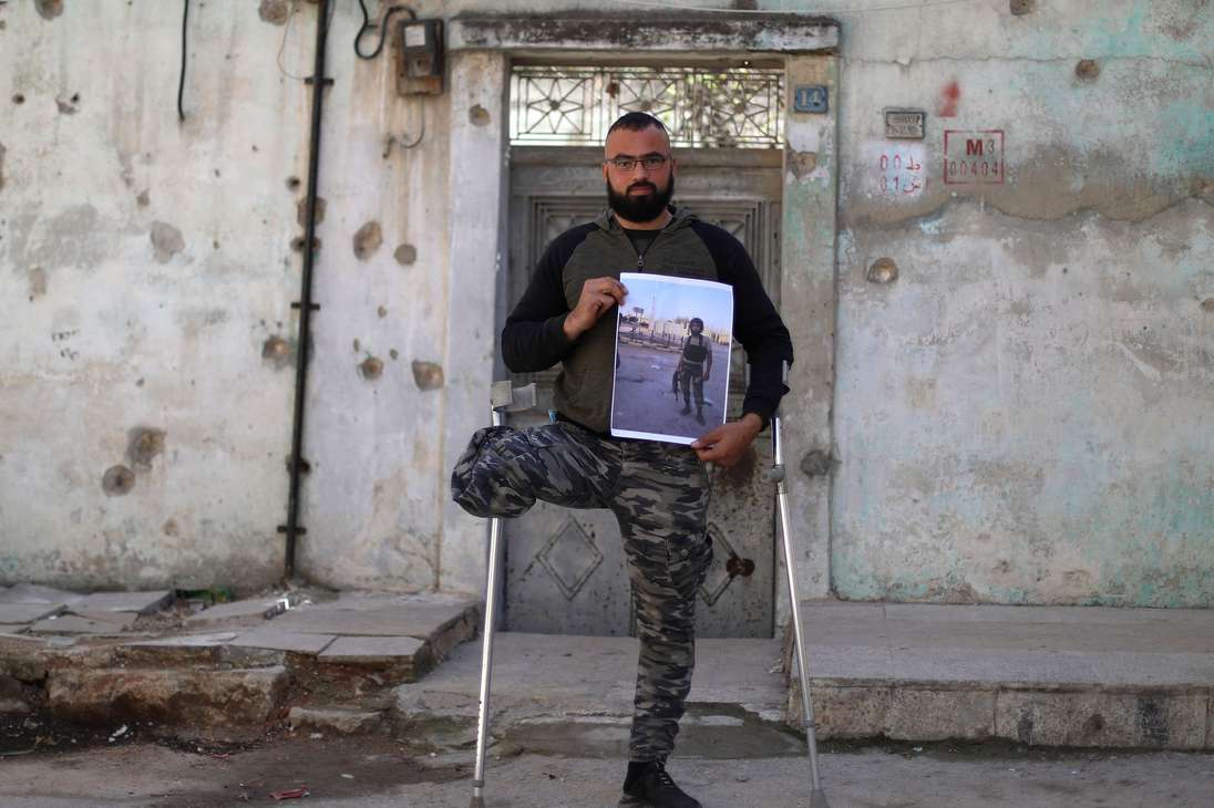 Mohammed al-Hamid, un excombatiente rebelde sirio de 28 años, posa para una foto mientras se apoya en muletas en la ciudad norteña de Idlib, controlada por los rebeldes, el 6 de marzo de 2021, mientras sostiene una foto de sí mismo  con uniforme militar y sosteniendo un arma. Hamid dice que fue herido en una batalla de 2016 contra las fuerzas gubernamentales en Latakia, donde su hermano también murió en sus brazos. Ese mismo año, se enteró de que otros tres hermanos habían muerto en prisión después de haber sido detenidos dos años antes. En 2017, aviones de guerra bombardearon su casa en Idlib y mataron a su hija.