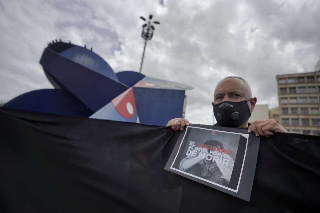 Un hombre, tras una tela negra, sostiene un cartel en el que se lee: el encierro es otra forma de morir.