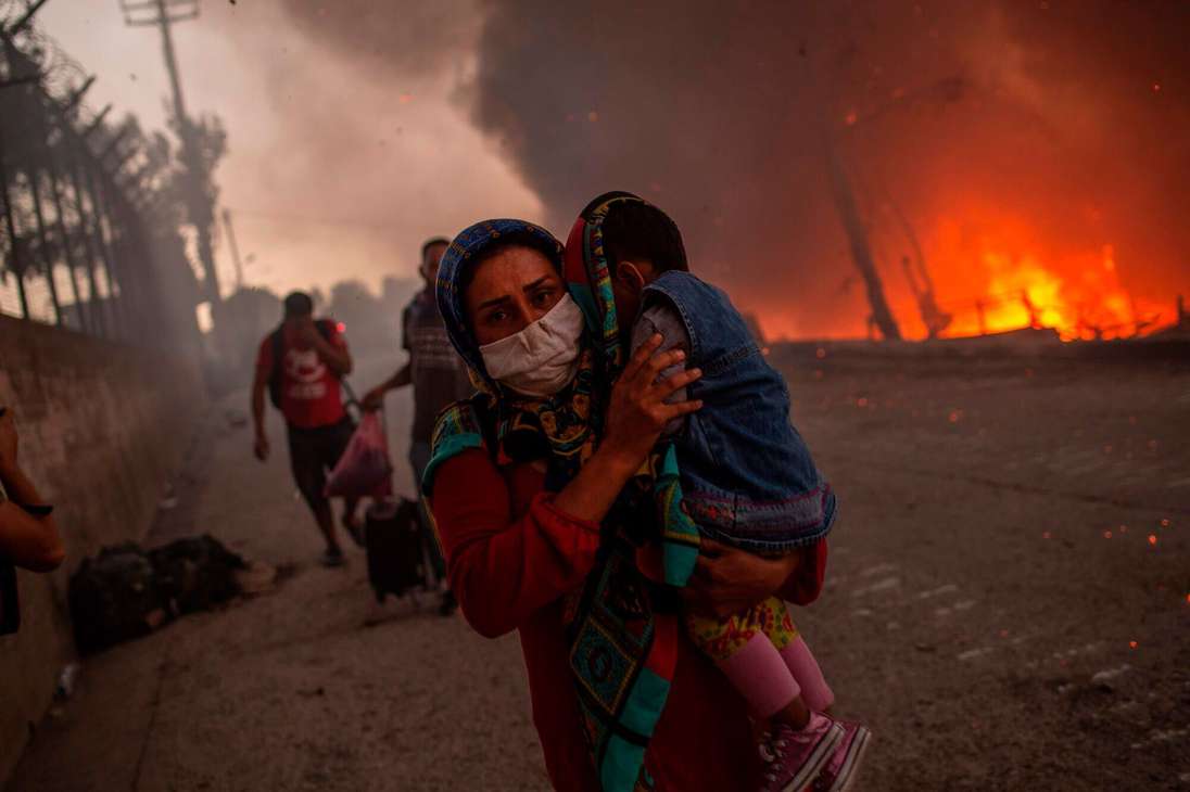 Una mujer lleva a un niño más allá de las llamas después de que estallara un gran incendio en el campamento de migrantes más grande de Grecia, en la isla griega de Lesbos, el 9 de septiembre de 2020.