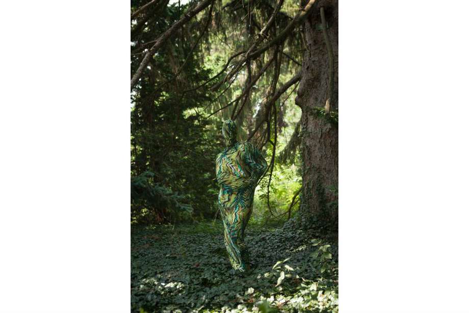 Container, obra de Joiri Minaya, quien muestra a una mujer con un traje tropical estampado, camuflándose en el entorno natural como una "alegoría de pertenencia".