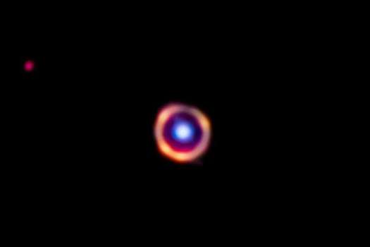 Una galaxia (azul; coloreada artificialmente) ayudó a que el James Webb observara mejor las moléculas orgánicas (puntos anaranjados brillantes) de una segunda galaxia.