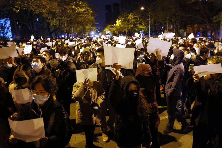 Manifestantes marchan sosteniendo papeles blancos durante una protesta provocada por un incendio en Urumqi que mató a 10 personas en Pekín, China.