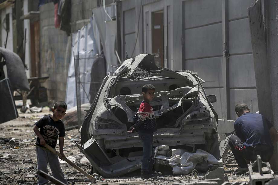 Hombre palestino con dos niños entre edificios destruidos cerca de un automóvil dañado en el campo de refugiados de Al Maghazi, en el centro de la Franja de Gaza, el 15 de abril de 2024, tras los ataques aéreos israelíes.
