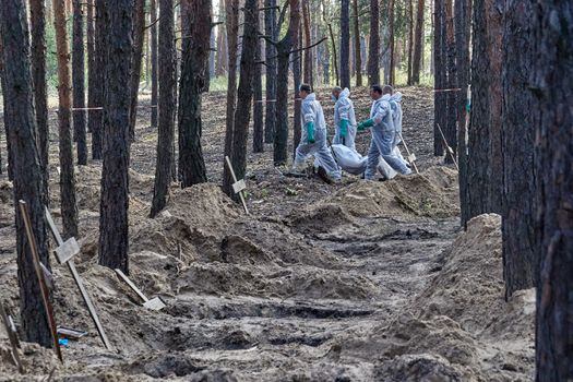 Trabajadores ucranianos cargan un cuerpo que fue desenterrado de tumbas en Izyum, región de Kharkiv, noreste de Ucrania.