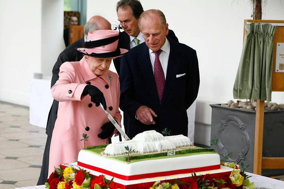 La reina Isabel II corta un pastel como el príncipe Felipe