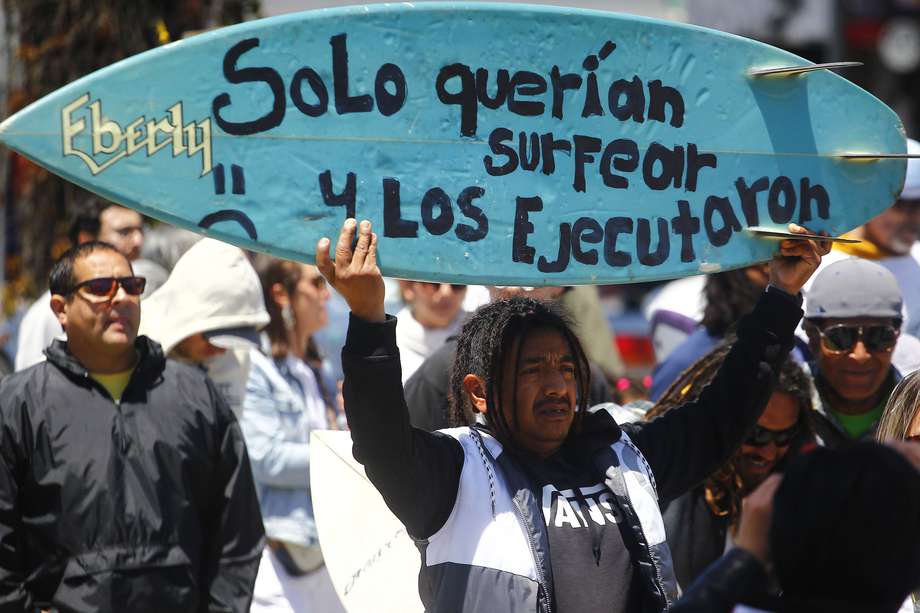 Un hombre sostiene una tabla de surf durante una manifestación para exigir justicia por el asesinato de tres surfistas extranjeros este domingo, en la ciudad de Ensenada (México).